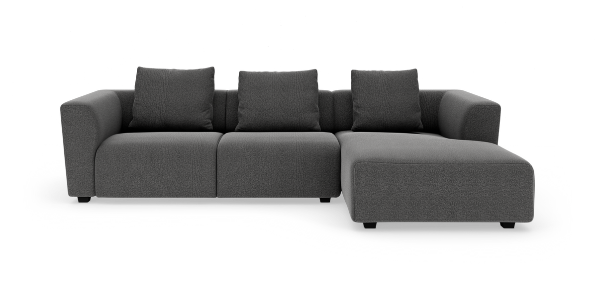 Mørkegrå modulsofa med chaiselong til højre og fire ryghynder, frilagt på hvid baggrund.