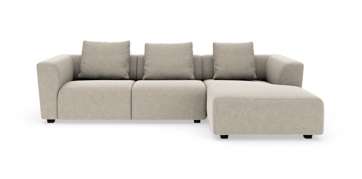 Beige hjørnesofa med chaiselong til højre, tre sæder og fire ryghynder, fritlagt på hvid baggrund.