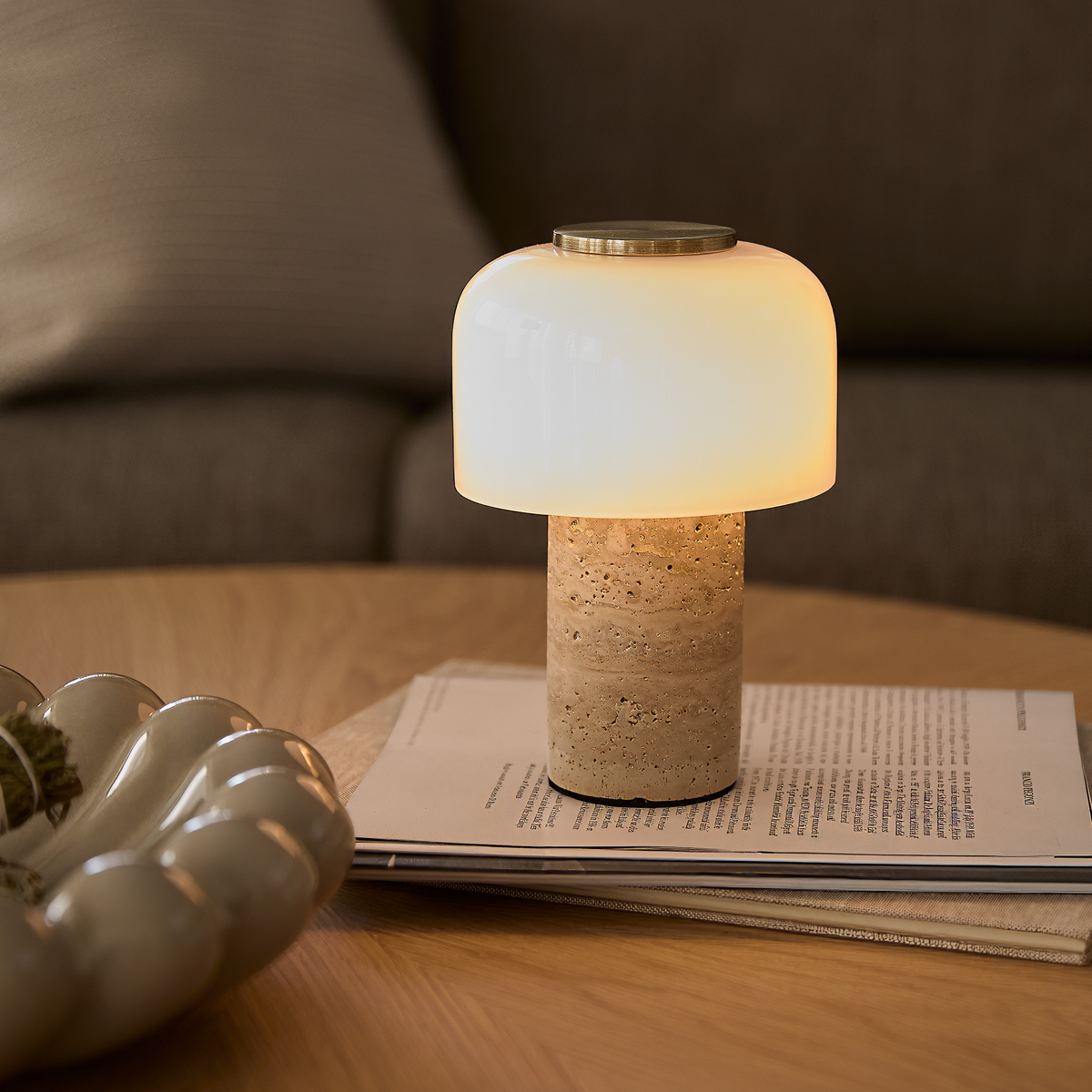 Bordlampe med hvid glaskuppel og stensokkel på sofabord i varm, hyggelig belysning.