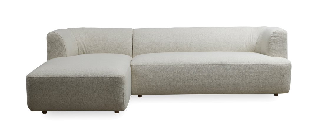 L‑formet lys beige hjørnesofa med venstrevendt chaiselong, bløde afrundede former i boucléstof, frilagt på mørk baggrund.