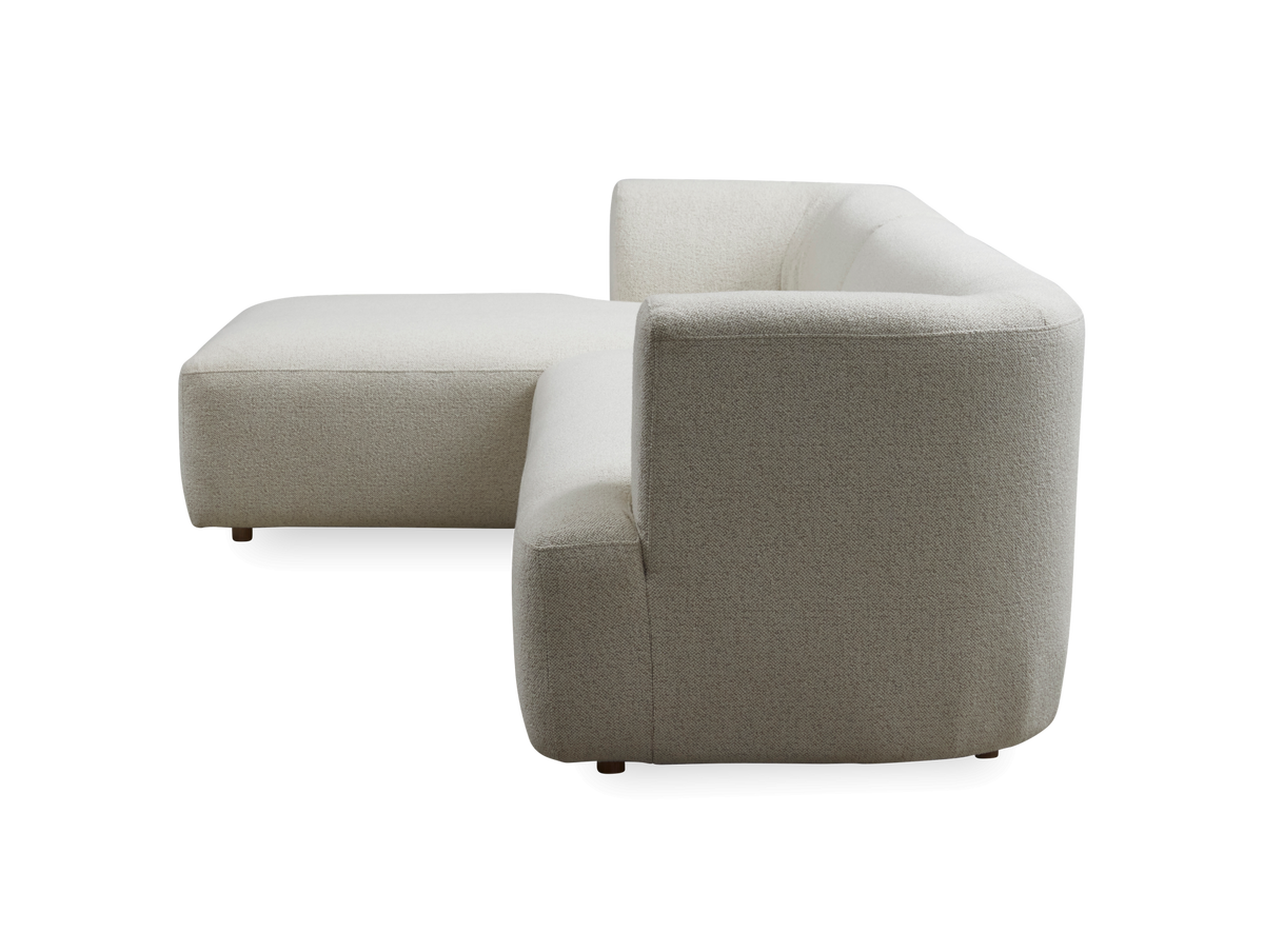 Lysebeige L‑formet modulsofa, set fra siden på frilagt baggrund.