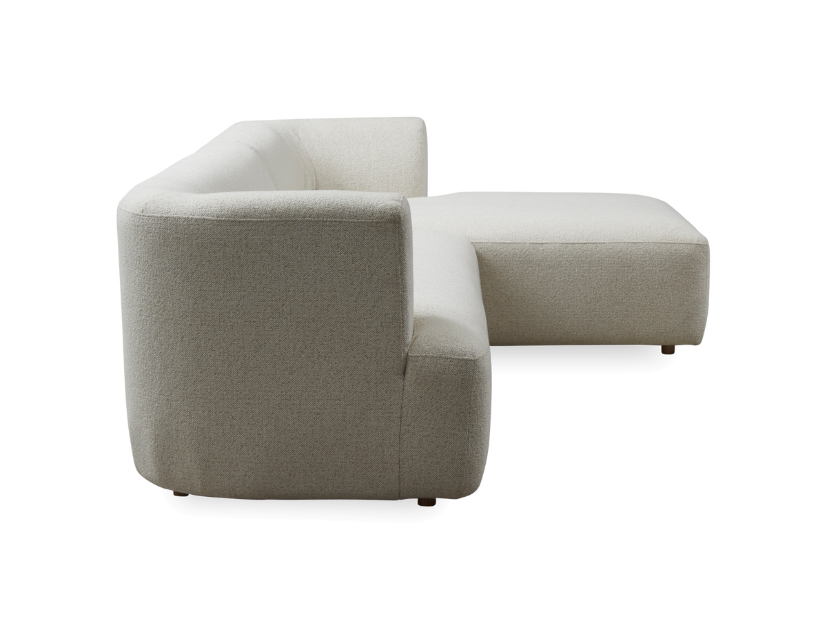 Beige L‑formet modulsofa i stof, set fra siden, fritlagt mod hvid baggrund.