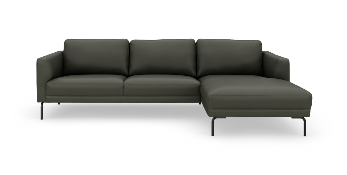 Mørkegrøn hjørnesofa med chaiselong til højre og slanke sorte ben, frilagt på hvid baggrund.