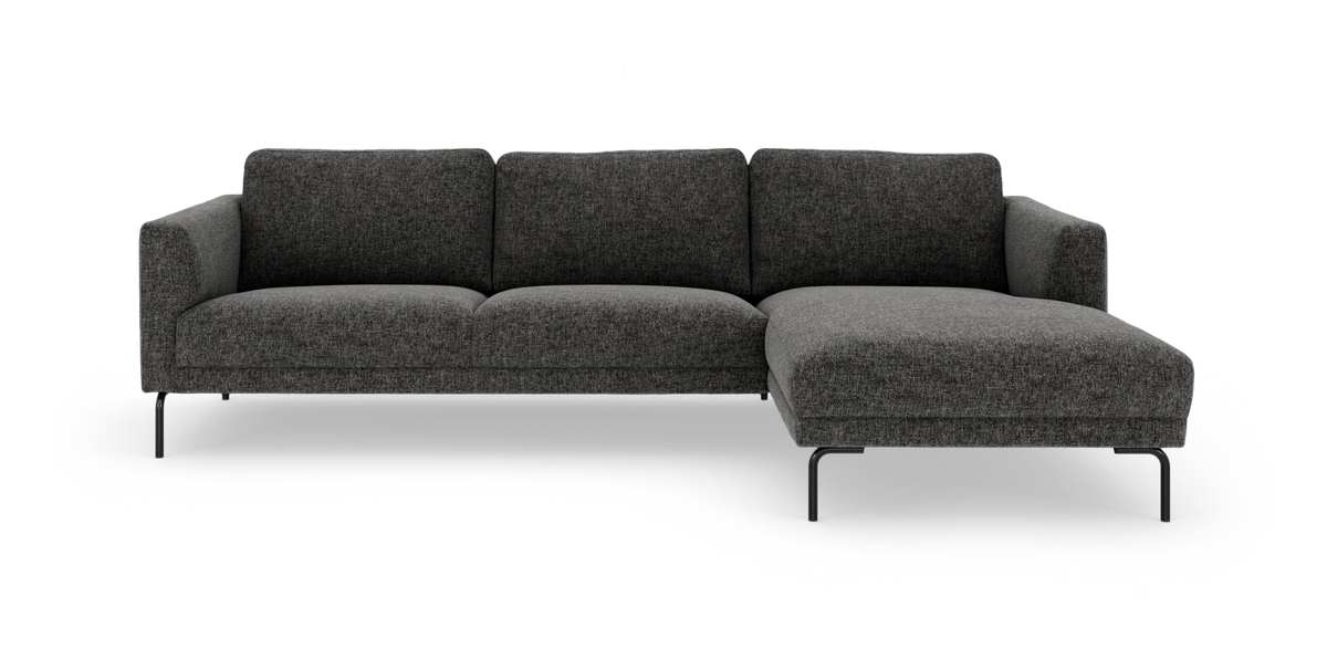 Mørkegrå hjørnesofa med chaiselong i højre side på slanke sorte ben, frilagt mod hvid baggrund.