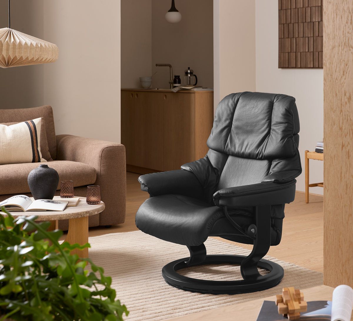 Sort læderlænestol i skandinavisk stue med beige sofa, træbord, planter og lyst tæppe.