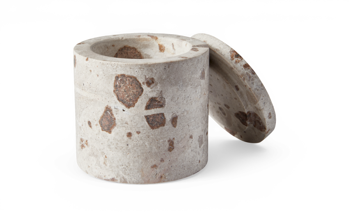 Cylindrisk opbevaringskrukke i terrazzo/sten med aftaget låg, grå med brune pletter, frilagt på hvid baggrund.
