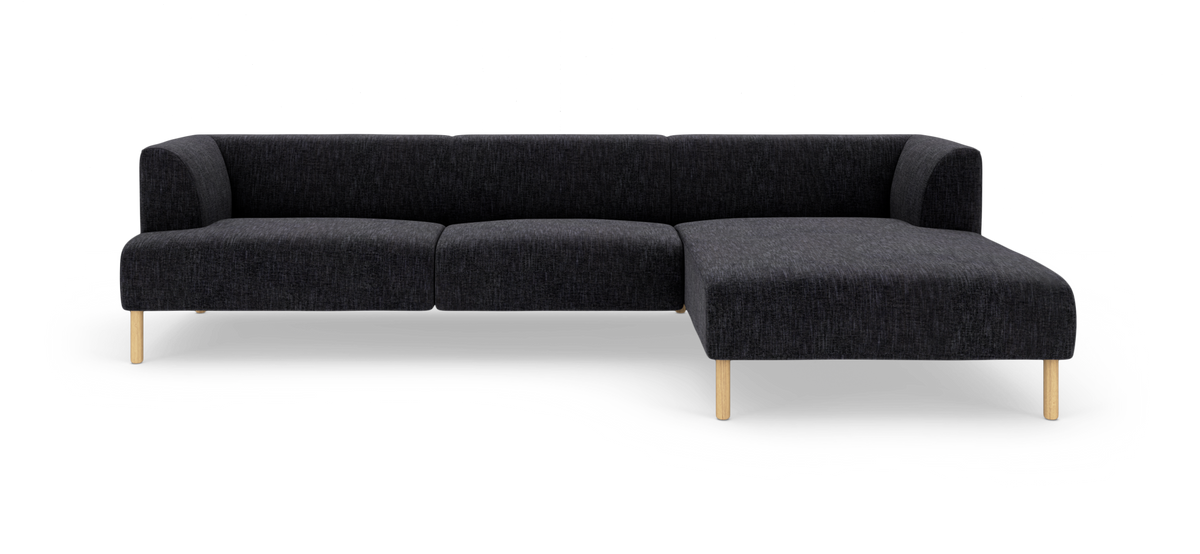 Mørkegrå hjørnesofa med chaiselong til højre og lyse træben, frilagt på hvid baggrund.