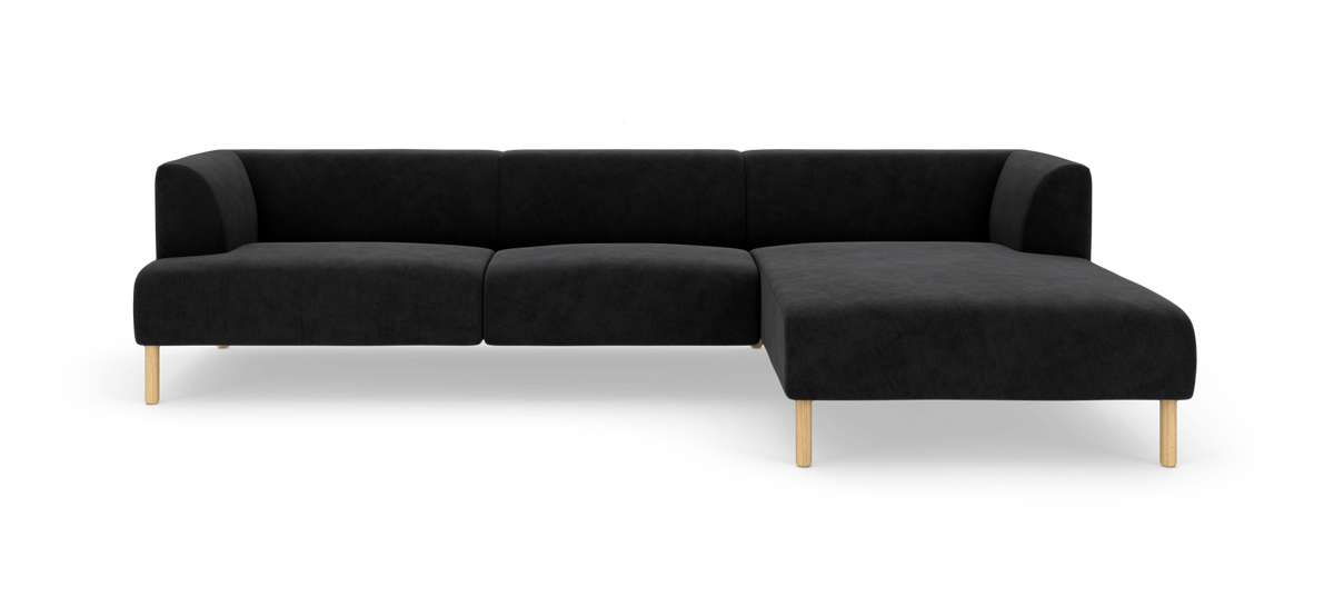 Sort modulsofa med chaiselong til højre og lyse træben, fotograferet forfra på hvid baggrund.
