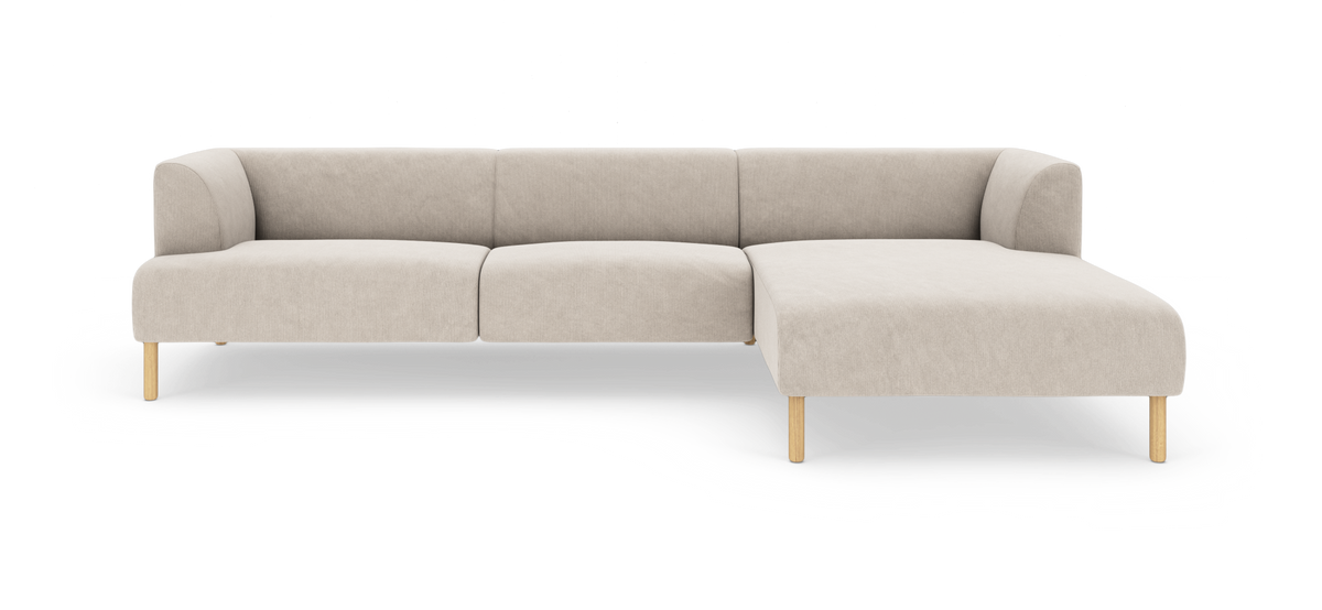 Beige L-formet modulsofa med chaiselong til højre og lyse træben, fotograferet forfra på hvid baggrund.