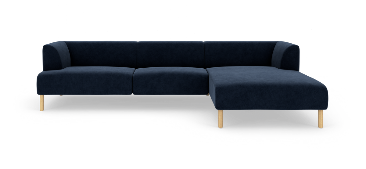 Mørkeblå modulsofa med chaiselong til højre og lyse træben, frilagt på hvid baggrund.