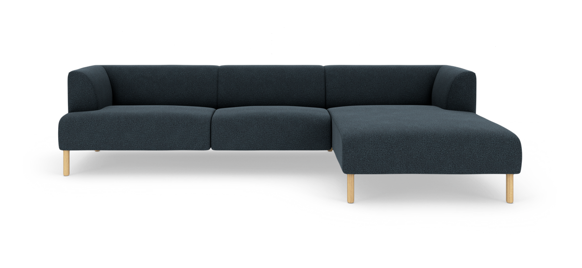 Mørkeblå L-sofa med chaiselong til højre og lyse træben, frilagt på hvid baggrund.