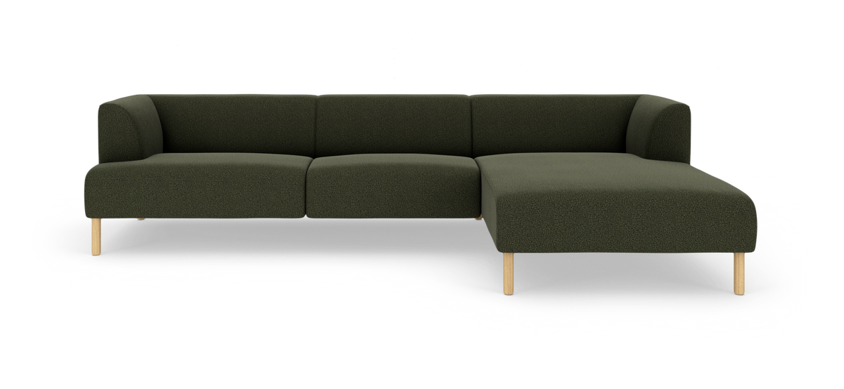 Modulær hjørnesofa i mørkegrønt tekstil med højre chaiselong og lyse træben, fritlagt på hvid baggrund.