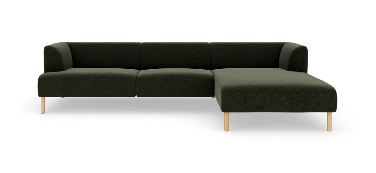 Mørkegrøn modulsofa med chaiselong på højre side og lyse træben, set forfra mod hvid baggrund.