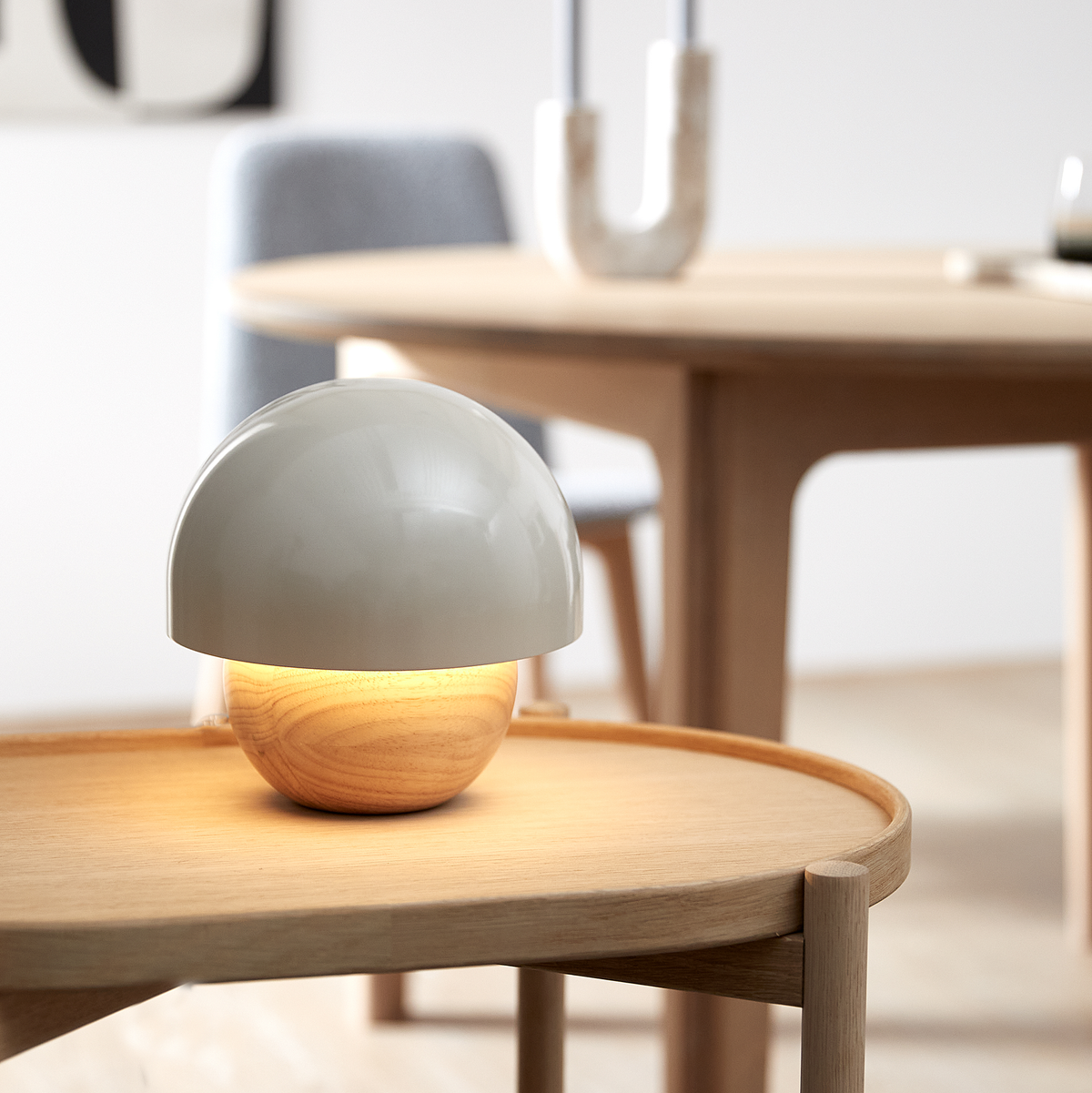 Lille bordlampe med hvid halvkugle og træfod, der lyser varmt på et lyst træbord i et skandinavisk spisemiljø.
