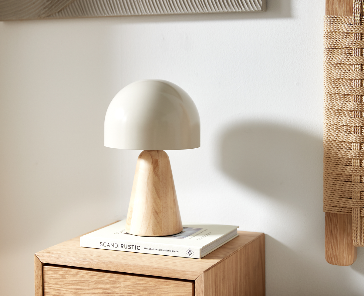 Beige bordlampe med træfod står på ”Scandi Rustic” af Rebecca Lawson & Reena Simon på et skab i lyst træ i et lyst, luftigt rum.