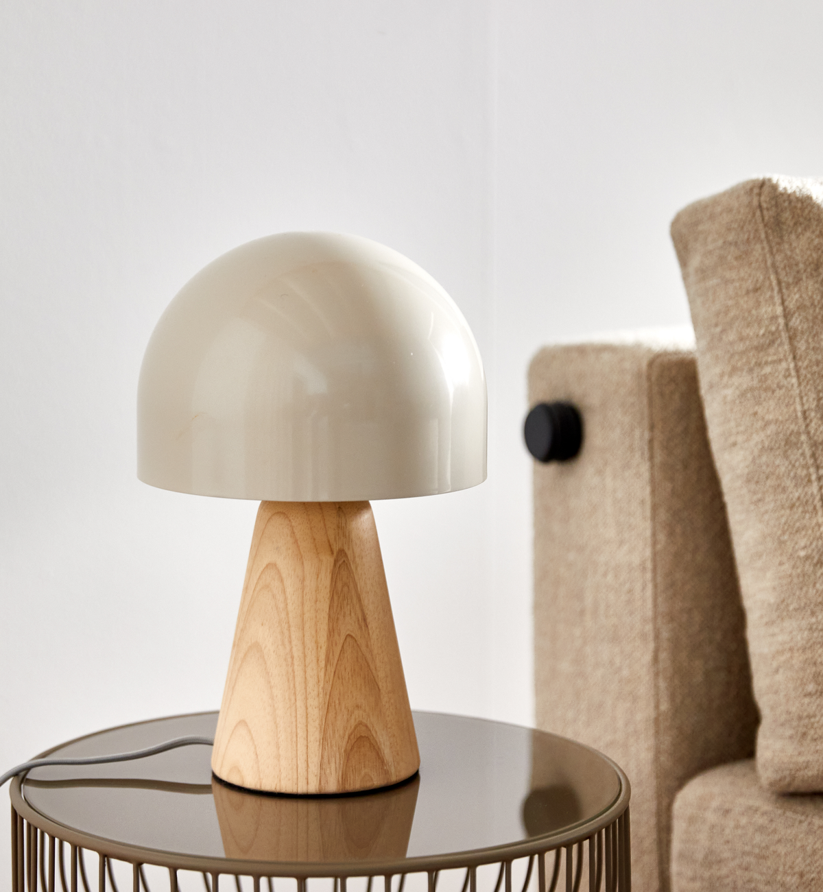 Bordlampe med cremefarvet kuppel og træfod på et rundt sidebord ved siden af en beige sofa i en lys stue.