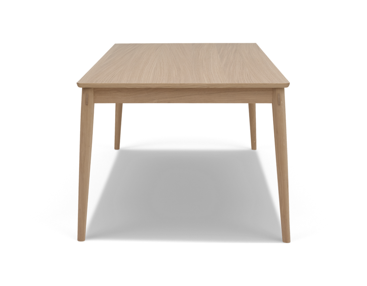 Rektangulært spisebord i lys eg med koniske ben, set forfra.