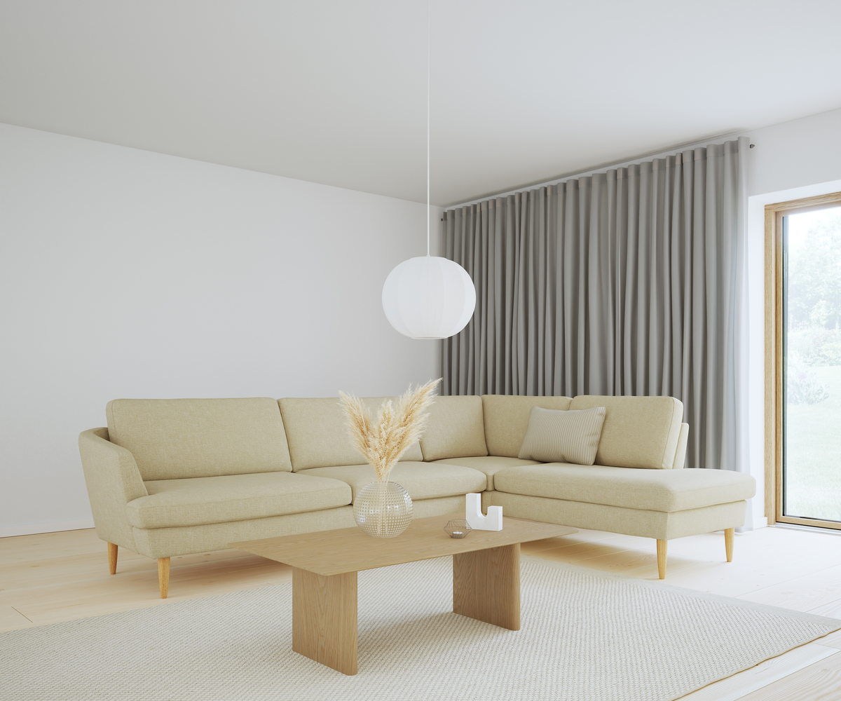 Lyst skandinavisk stue med beige hjørnesofa, træbord med pampas i glasvase, rund hvid pendellampe og grå gardiner ved stort vindue.