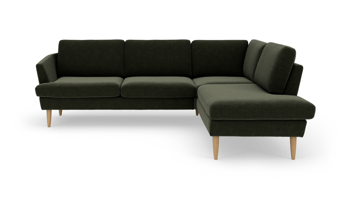Mørkegrøn L‑sofa med chaiselong til højre og lyse træben.