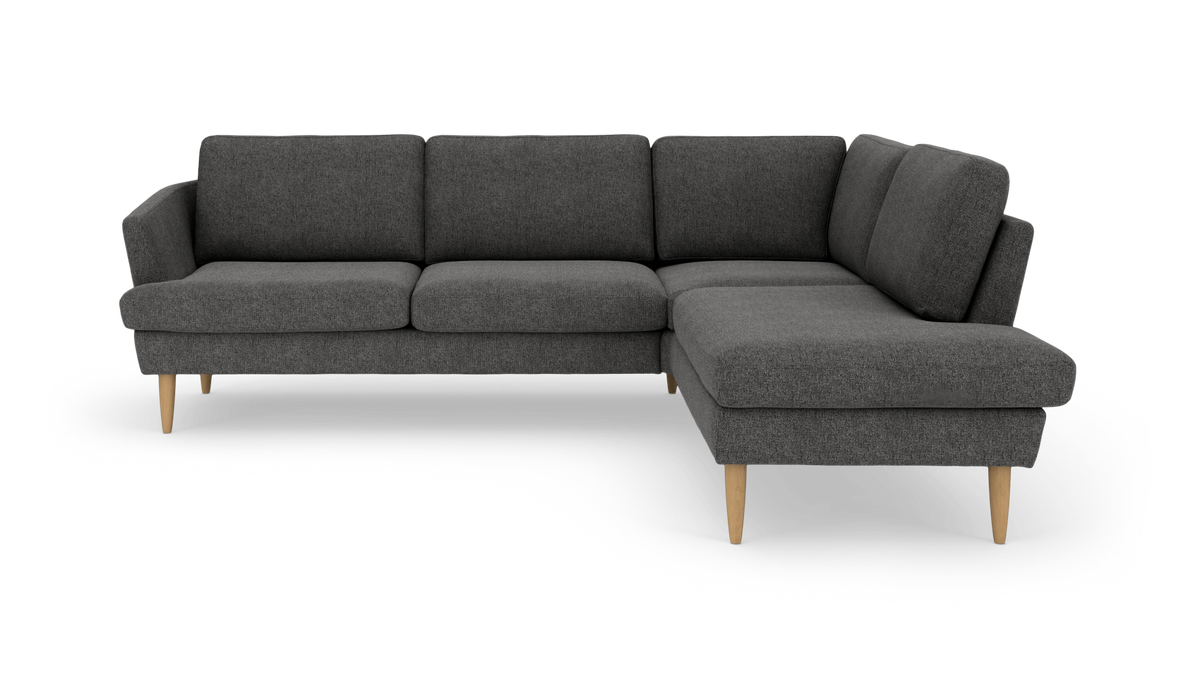 Mørkegrå hjørnesofa med chaiselong til højre og lyse træben, frilagt på hvid baggrund.