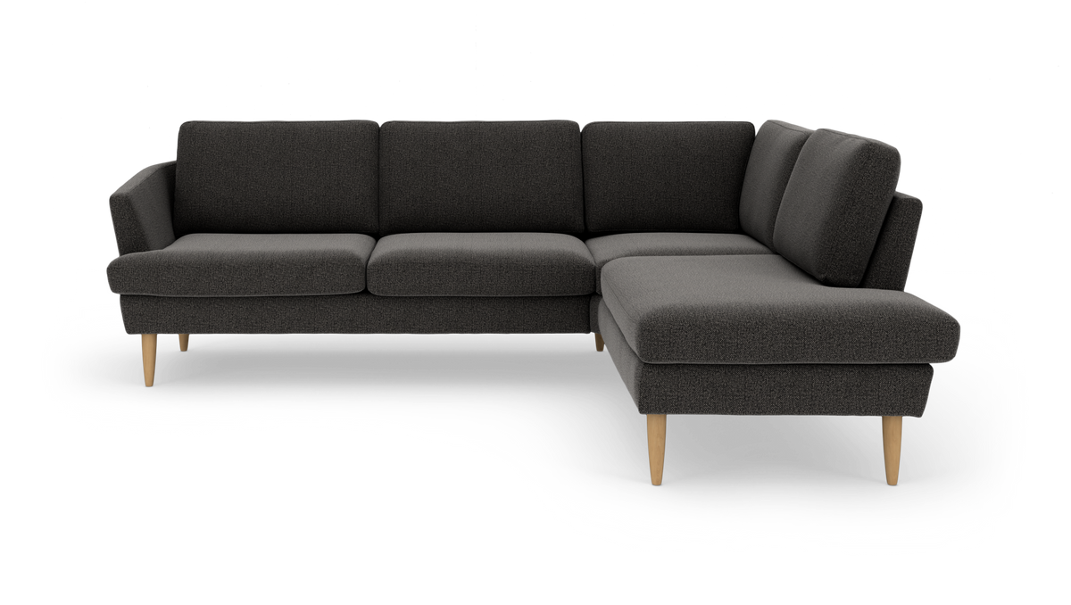 Mørkegrå hjørnesofa med chaiselong til højre og lyse træben, fritlagt på hvid baggrund.