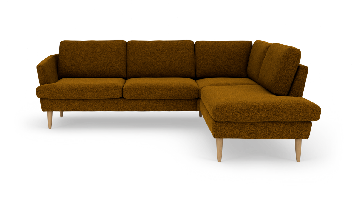 Mørk sennepsgul L‑formet hjørnesofa med chaiselong til højre og slanke træben, frilagt i studie.