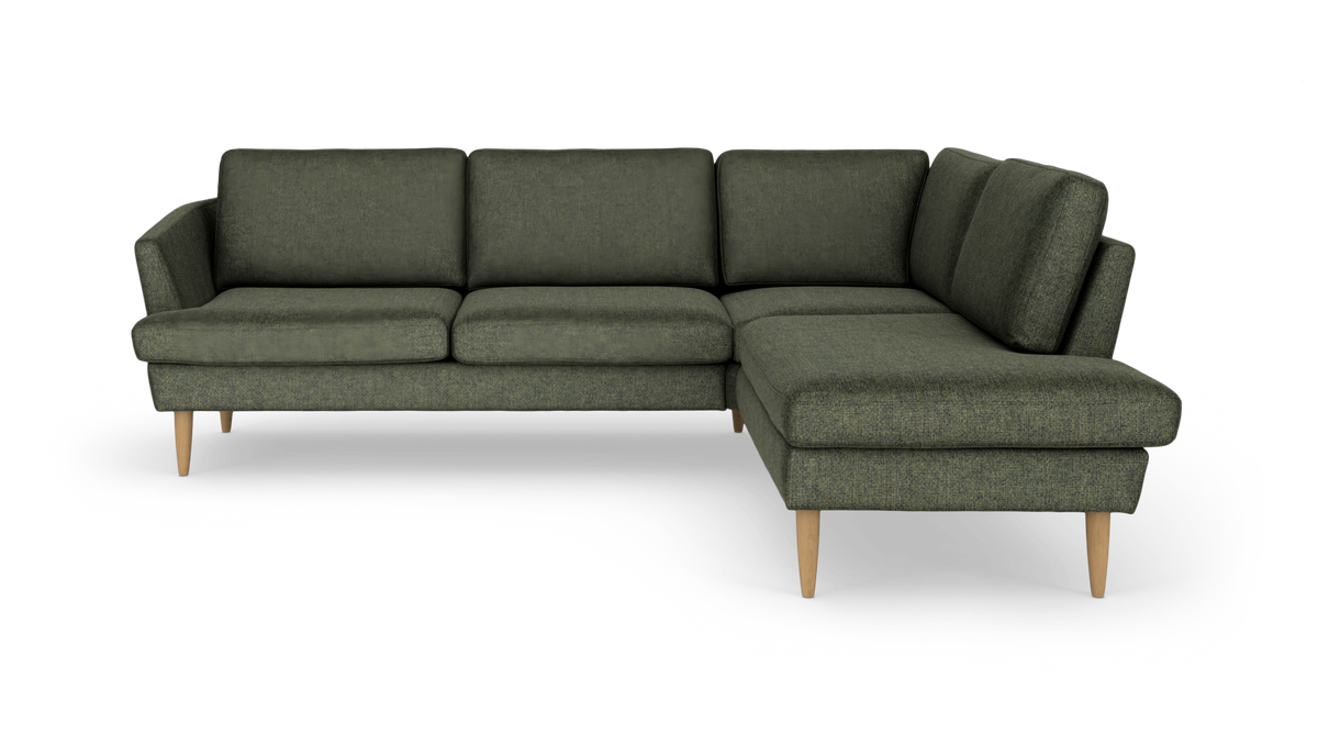 Grøn L‑sofa med chaiselong til højre og lyse træben, fritlagt.