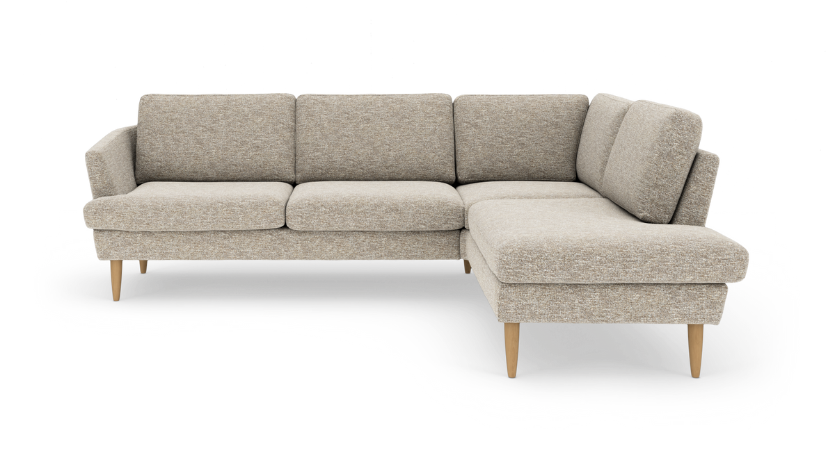 Beige L-formet hjørnesofa med chaiselong til højre og lyse, koniske træben, fotograferet lige forfra på hvid studiebaggrund.