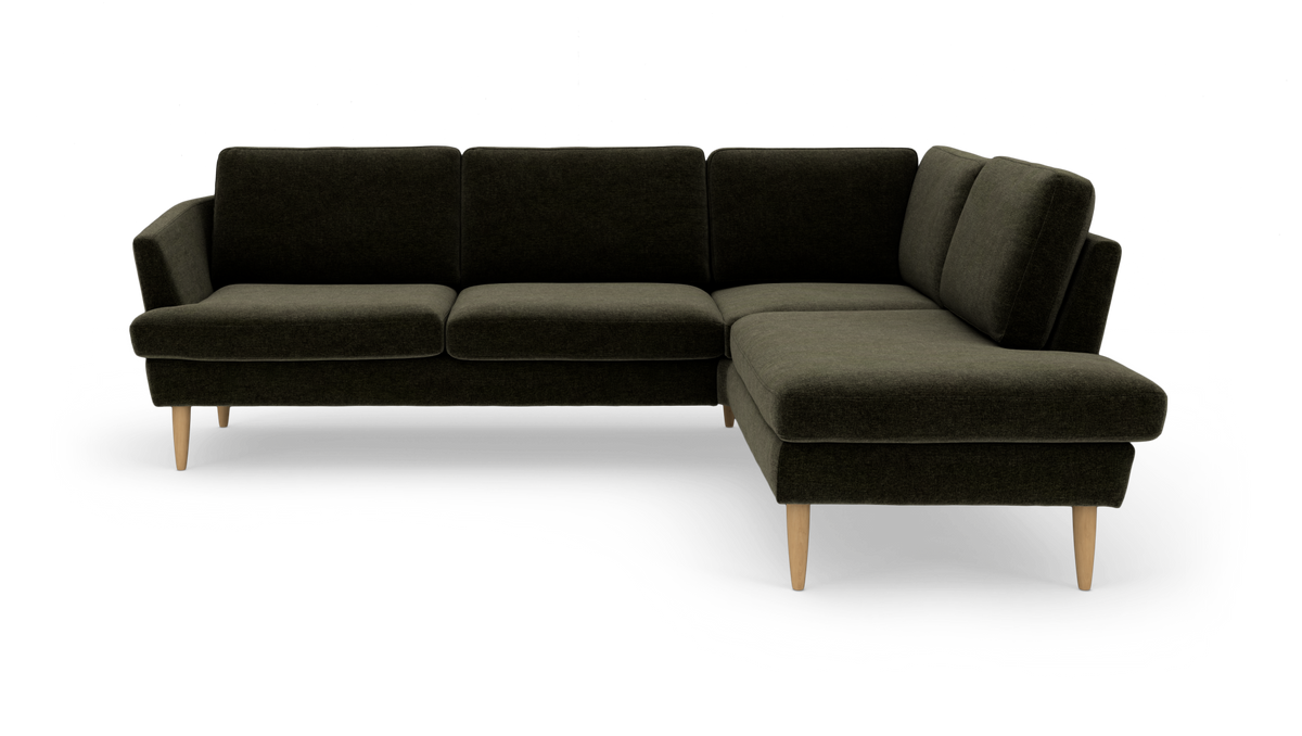 Mørkegrøn L‑sofa med chaiselong til højre og lyse træben, frilagt på hvid baggrund.