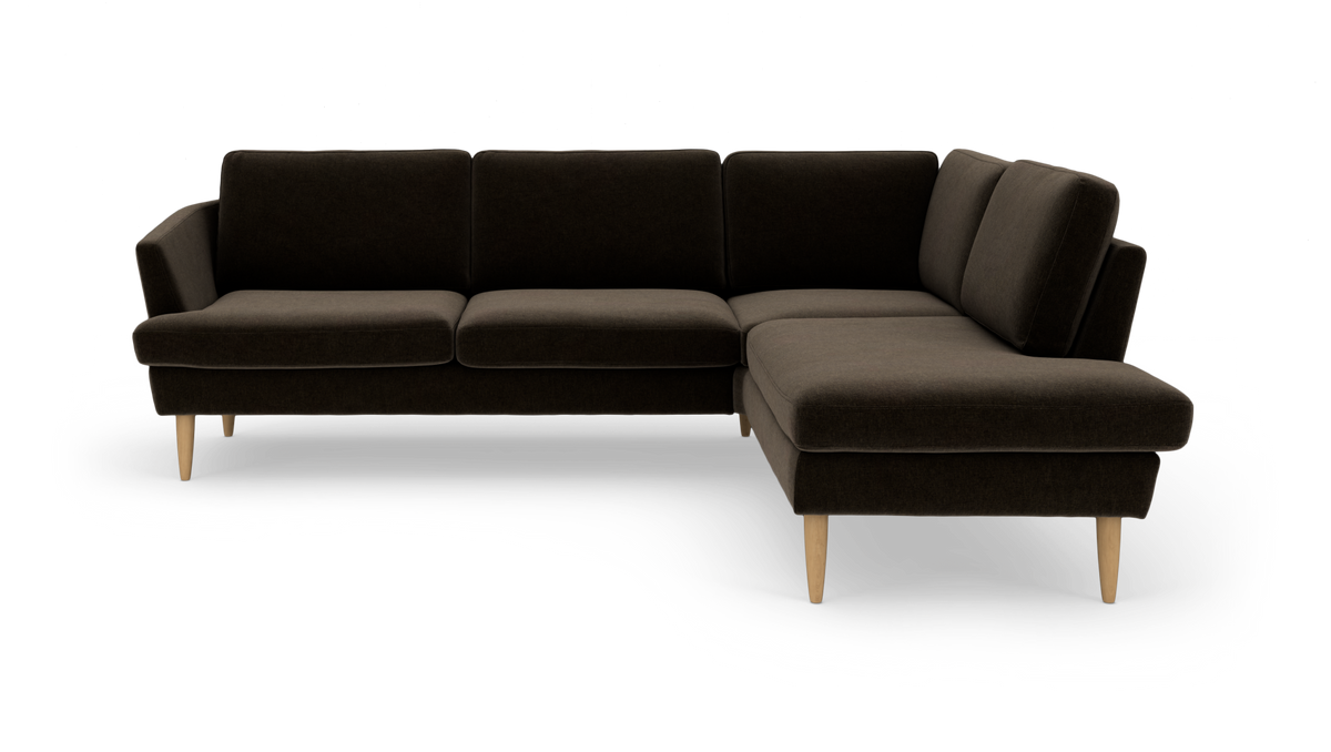 Mørkebrun hjørnesofa med chaiselong til højre og lyse træben, frilagt på hvid baggrund.