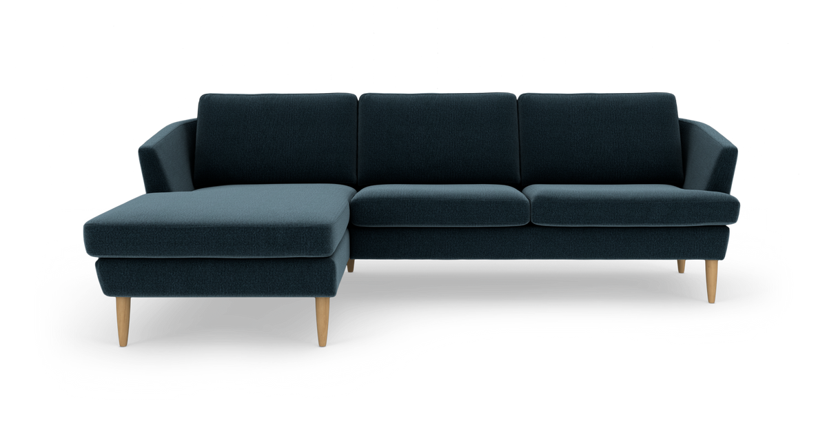 Mørk blågrøn sofa med venstre chaiselong og lyse træben, frilagt på hvid baggrund.