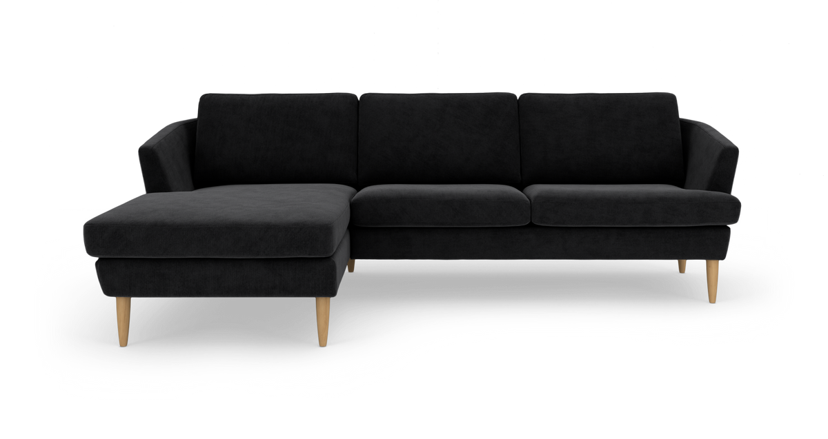 Sort hjørnesofa med venstrevendt chaiselong og lyse træben, frilagt på hvid baggrund.