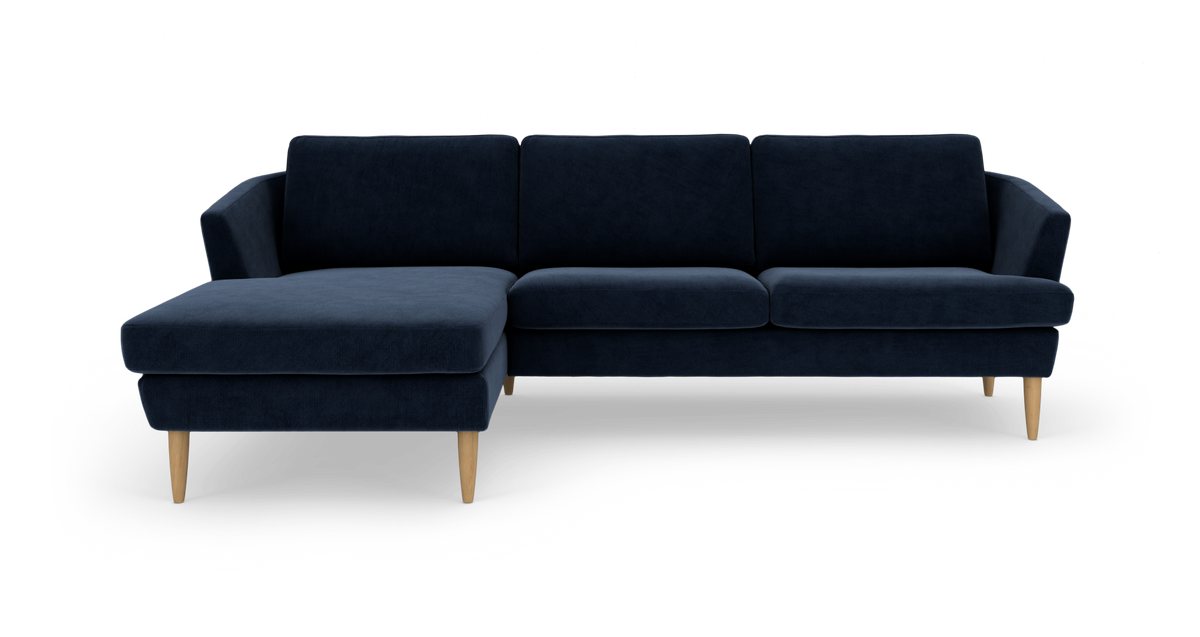 Mørkeblå hjørnesofa med venstre chaiselong og koniske træben, fritlagt på hvid baggrund.