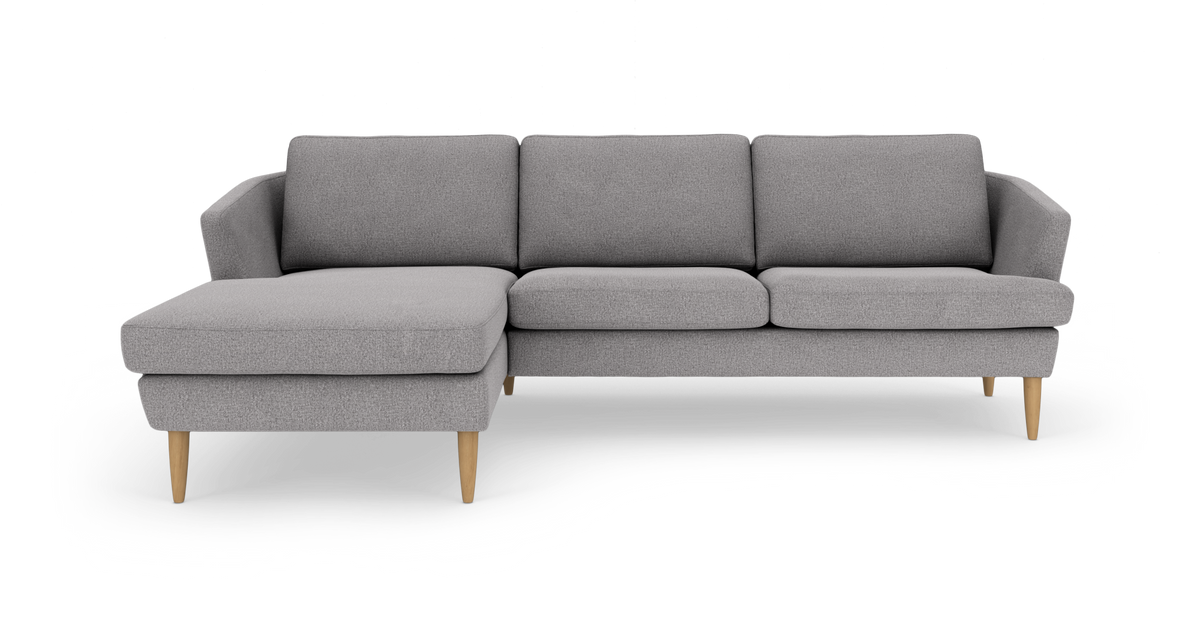 Grå hjørnesofa med venstrevendt chaiselong og lyse træben, frilagt på hvid baggrund.