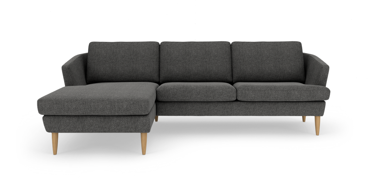 Mørkegrå hjørnesofa med venstre chaiselong, afrundede armlæn og lyse træben, frilagt på hvid baggrund.