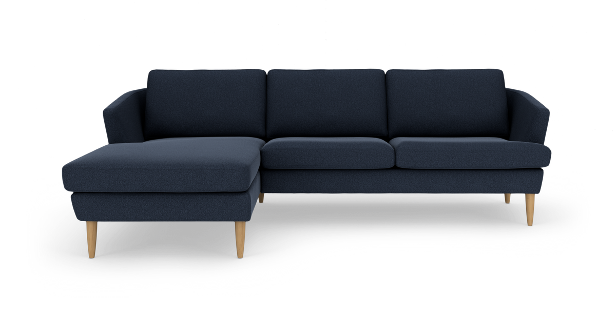Mørkeblå hjørnesofa med venstrevendt chaiselong og lyse træben, frilagt på hvid baggrund.