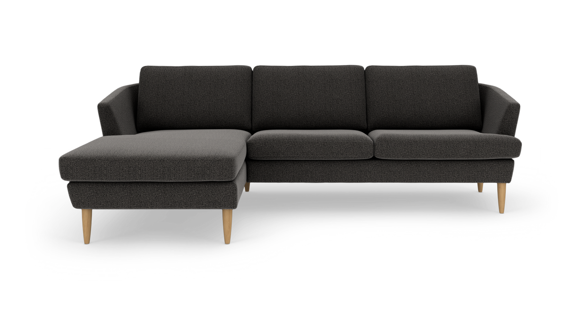 Mørkegrå hjørnesofa med venstrevendt chaiselong og koniske ben i lyst træ, frilagt på hvid baggrund.