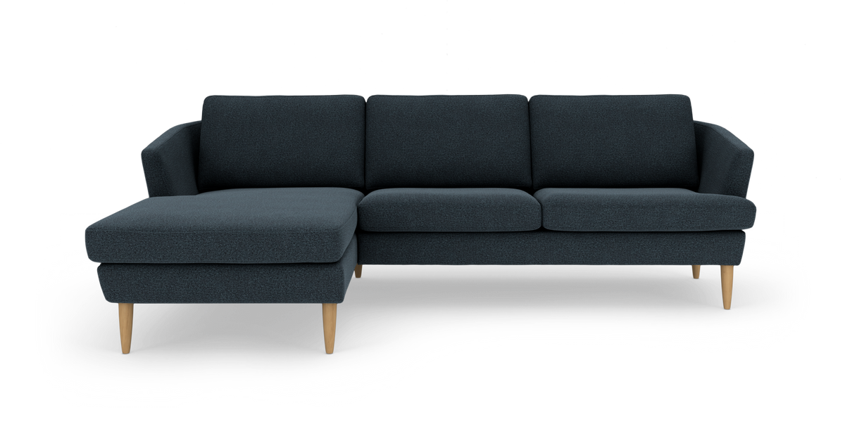 Mørkeblå hjørnesofa med chaiselong til venstre og lyse træben, set forfra.