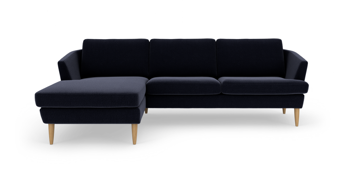 Mørkeblå hjørnesofa med chaiselong til venstre og lyse træben, frilagt på hvid baggrund.