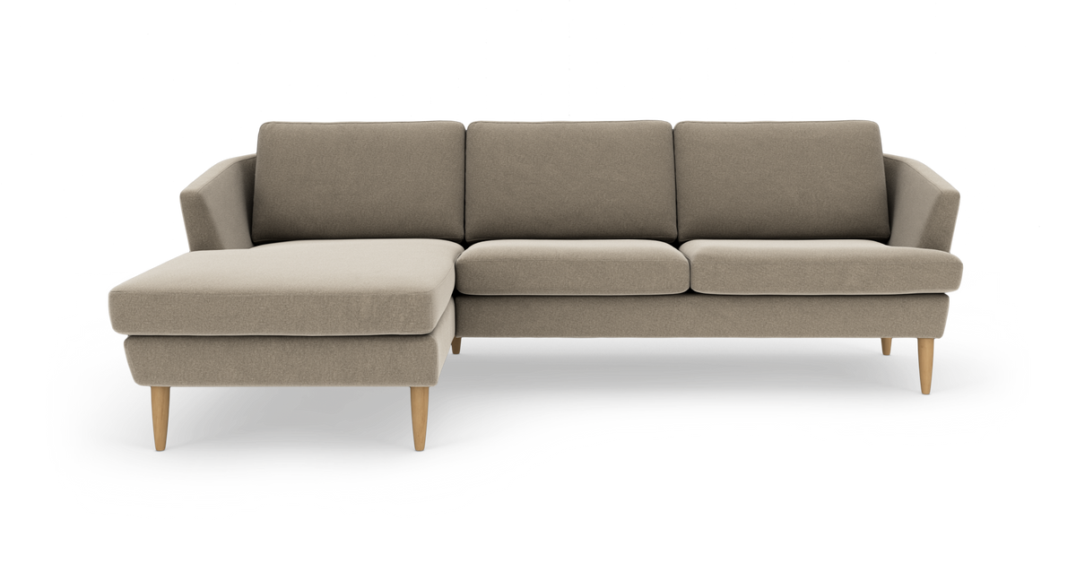 Beige modulsofa med venstre chaiselong og koniske træben, set forfra mod hvid baggrund.
