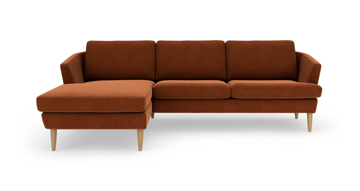 Rustfarvet hjørnesofa med venstrevendt chaiselong og lyse træben, frilagt på hvid baggrund.