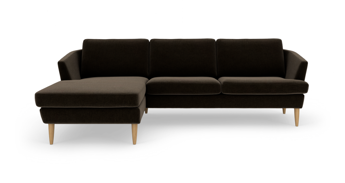 Mørkebrun hjørnesofa med venstrevendt chaiselong og lyse træben, set lige forfra på hvid baggrund.