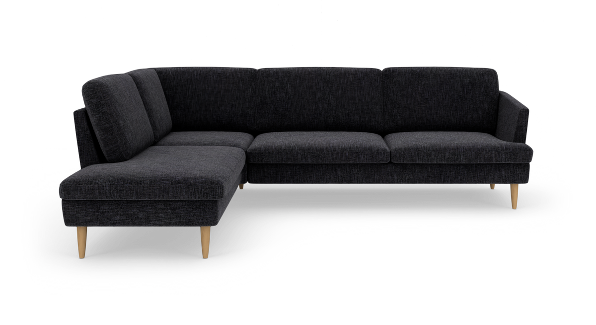 Mørkegrå L‑sofa med chaiselong til venstre og lyse træben, studiefoto.