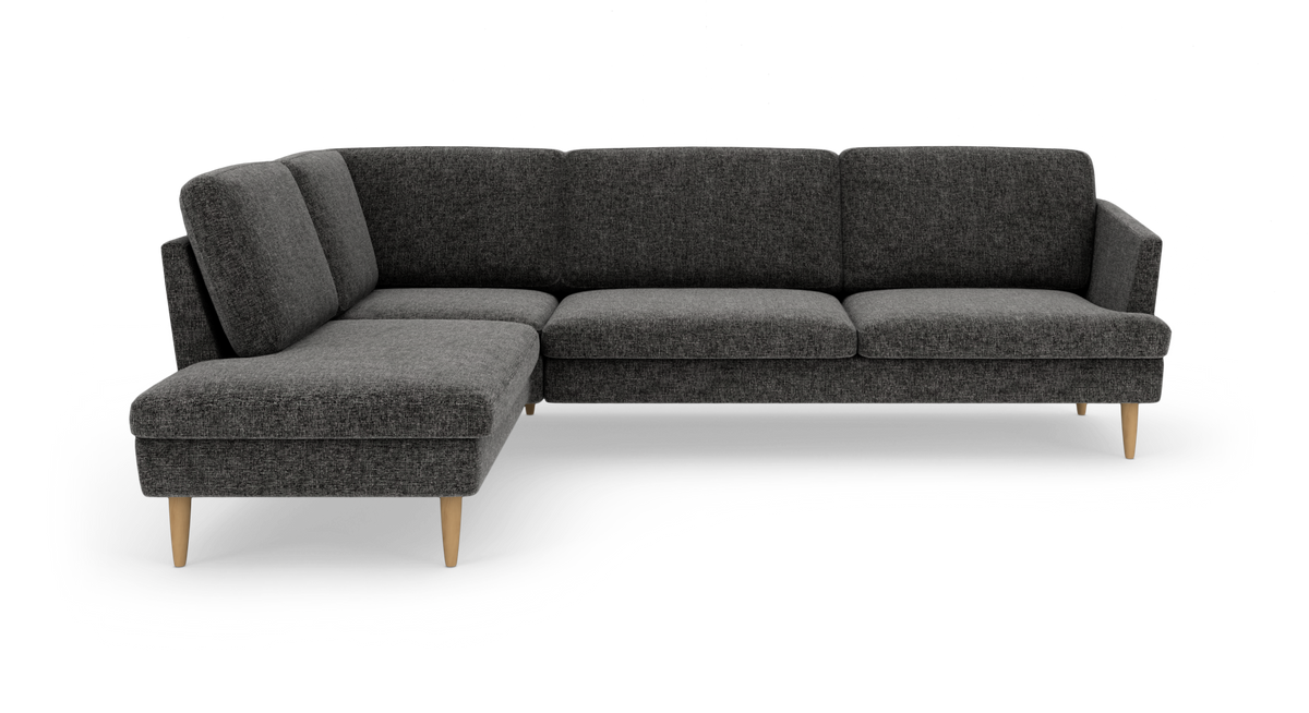 Mørkegrå L‑sofa i stof med træben, fotograferet i studie mod hvid baggrund.