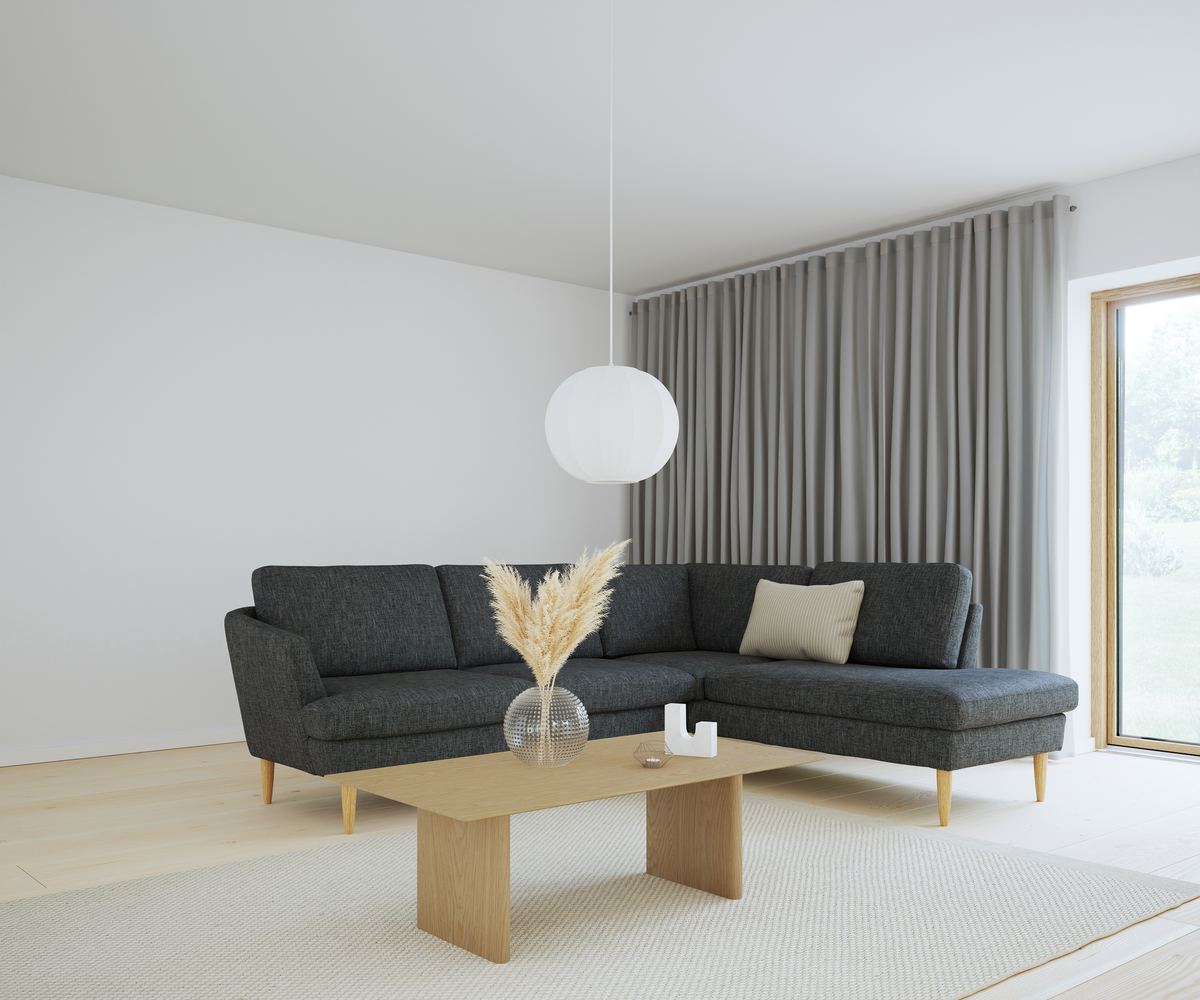 Lys stue med mørkegrå hjørnesofa, træbord med glasvase med pampasgræs, beige tæppe, grå gardiner og hvid rund pendellampe ved stort vindue.