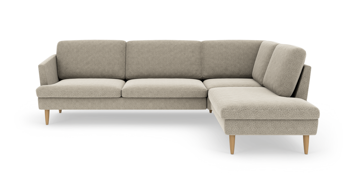 Beige L-formet hjørnesofa med chaiselong til højre og slanke træben i studiemiljø.