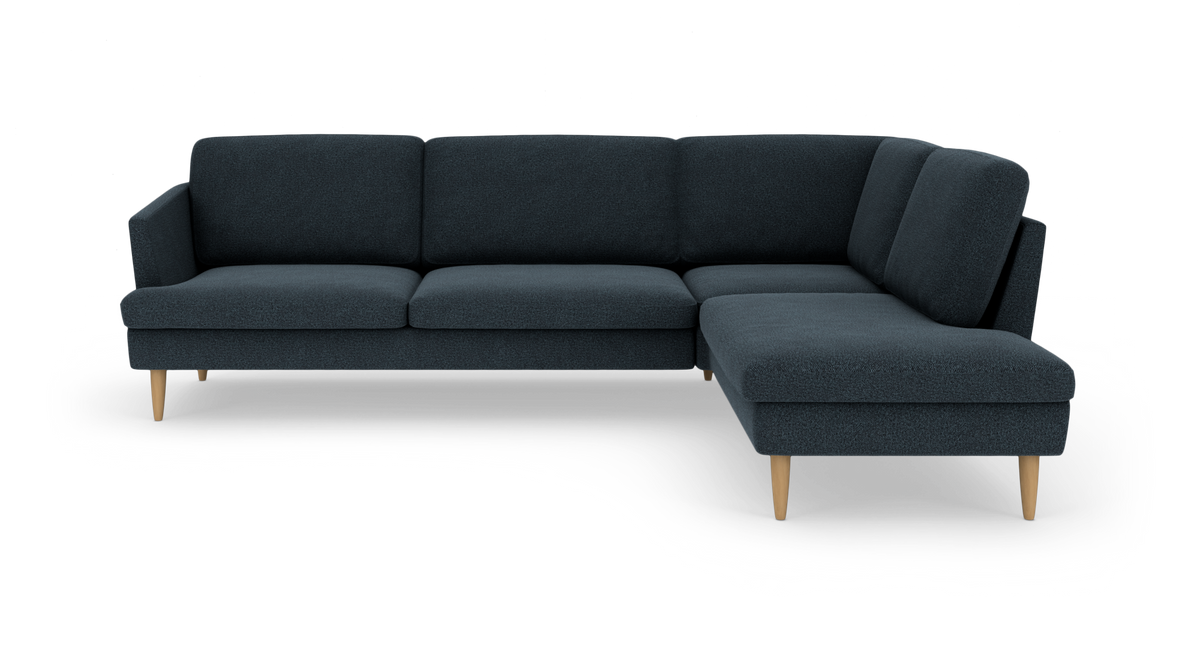 Mørkeblå hjørnesofa i stof med chaiselong til højre og lyse træben, frilagt på hvid baggrund.