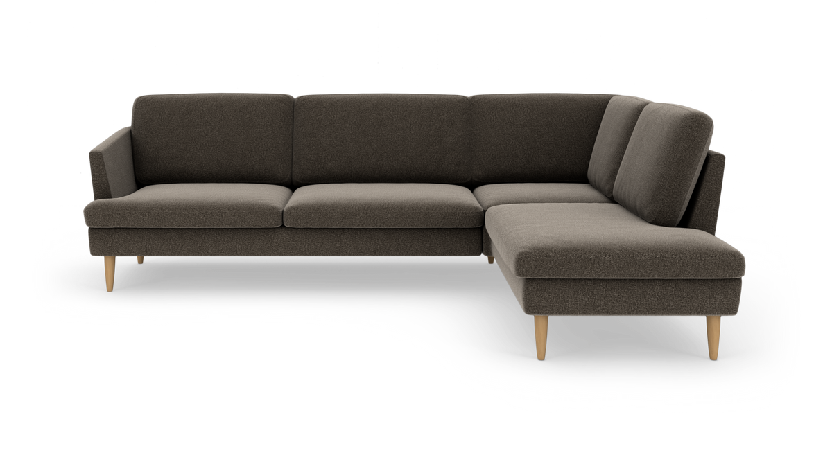 Mørkegrå hjørnesofa i stof med chaiselong til højre og lyse træben, frilagt mod hvid baggrund.