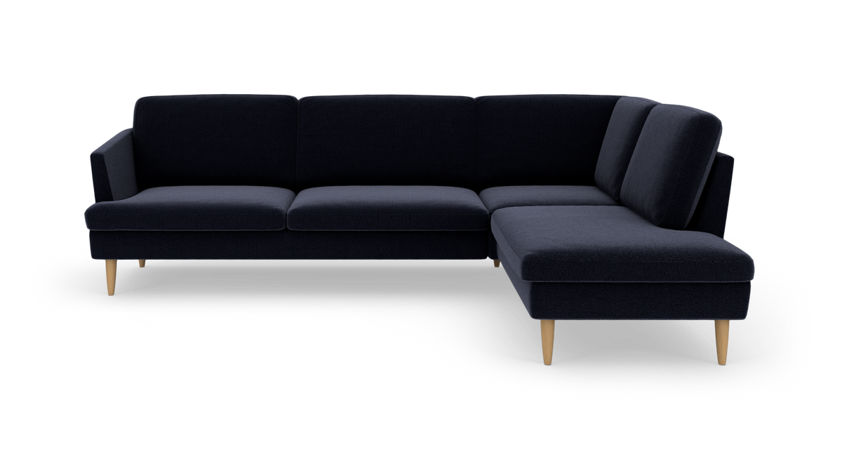 Mørkeblå L‑sofa med chaiselong til højre og lyse træben.