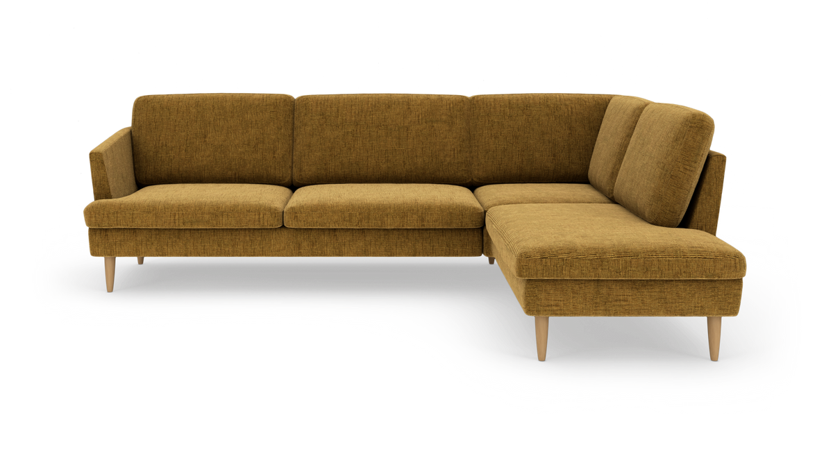 Sennepsgul L‑formet hjørnesofa med chaiselong til højre og lyse træben, frilagt i studielys.